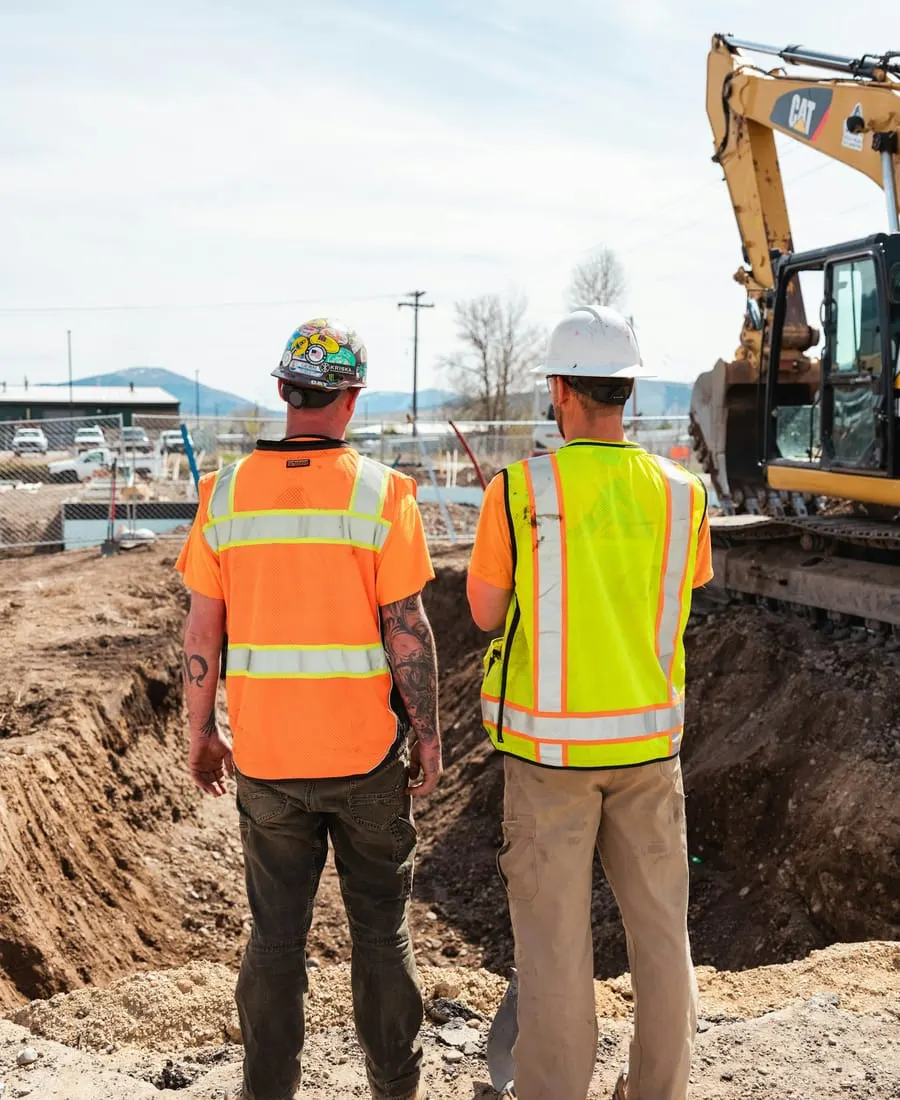 Two crew members in hi-vis vests overlooking an excavation site